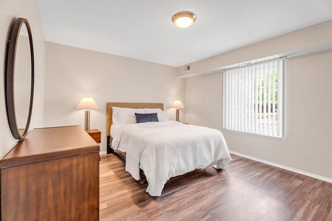 A bedroom with a bed, nightstand, and a round mirror on the wall.