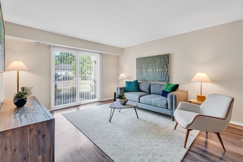A living room with a grey couch, a white chair, and a wooden side table.