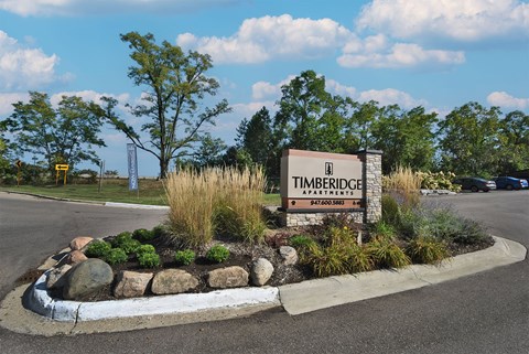 A sign for Timberidge Apartments is surrounded by plants and rocks.