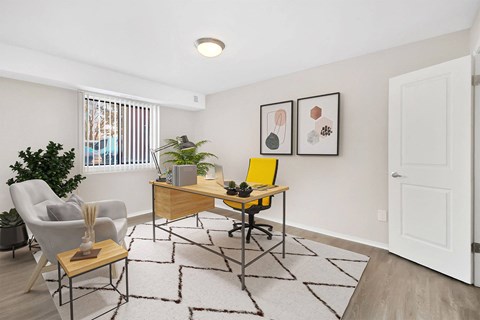 A room with a desk, chair, and potted plant.