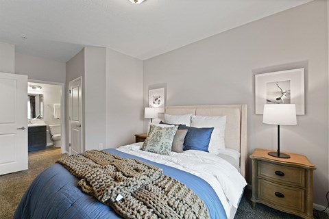A bedroom with a large bed and a lamp on a side table.