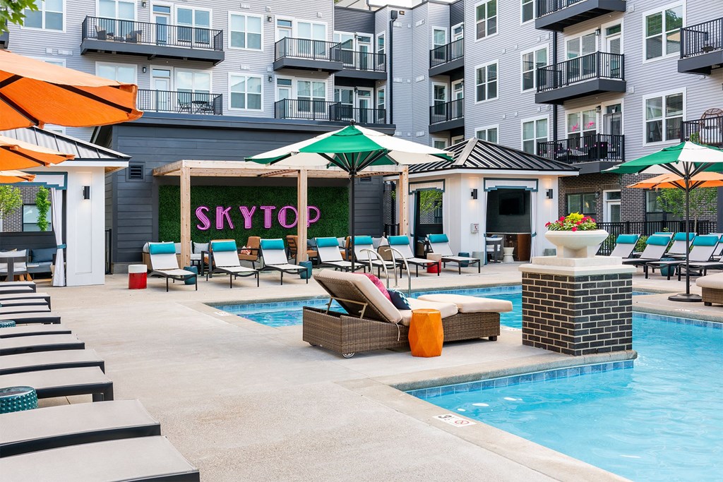 a swimming pool with lounge chairs and umbrellas in front of an apartment building