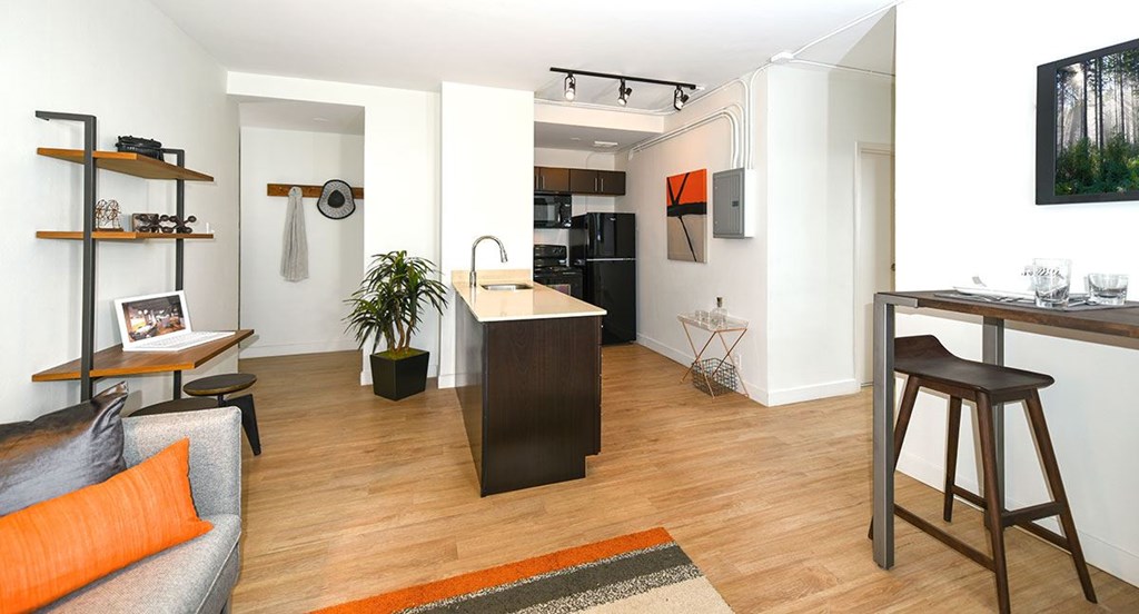 A modern kitchen with a wooden island and a grey couch with an orange pillow.