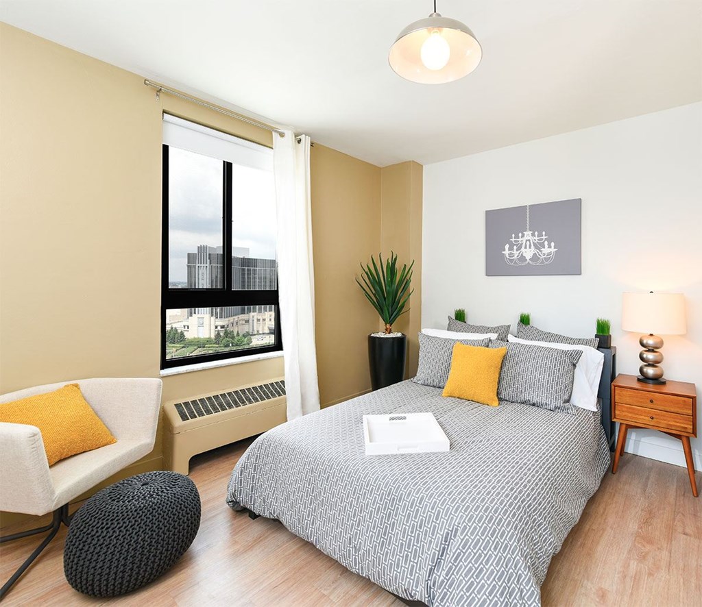 A bedroom with a large bed, a chair, and a window with a view of a cityscape.