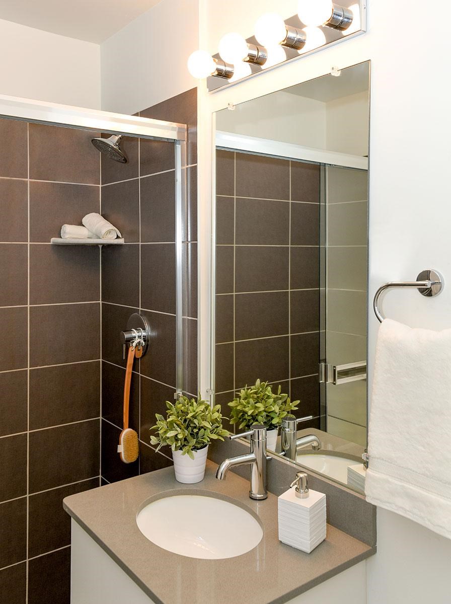 A bathroom with a brown tiled shower and a white sink.
