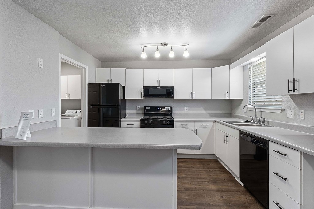 A kitchen with white cabinets and a black fridge.