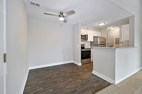 A room with a ceiling fan and a kitchen area in the background.