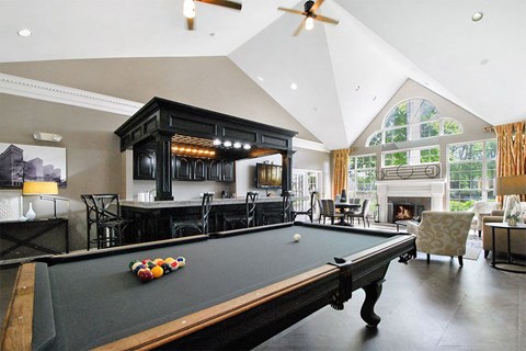 A pool table is in the middle of a room with a fireplace and a bar.
