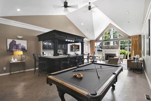 A pool table is in the middle of a room with a bar and a fireplace.