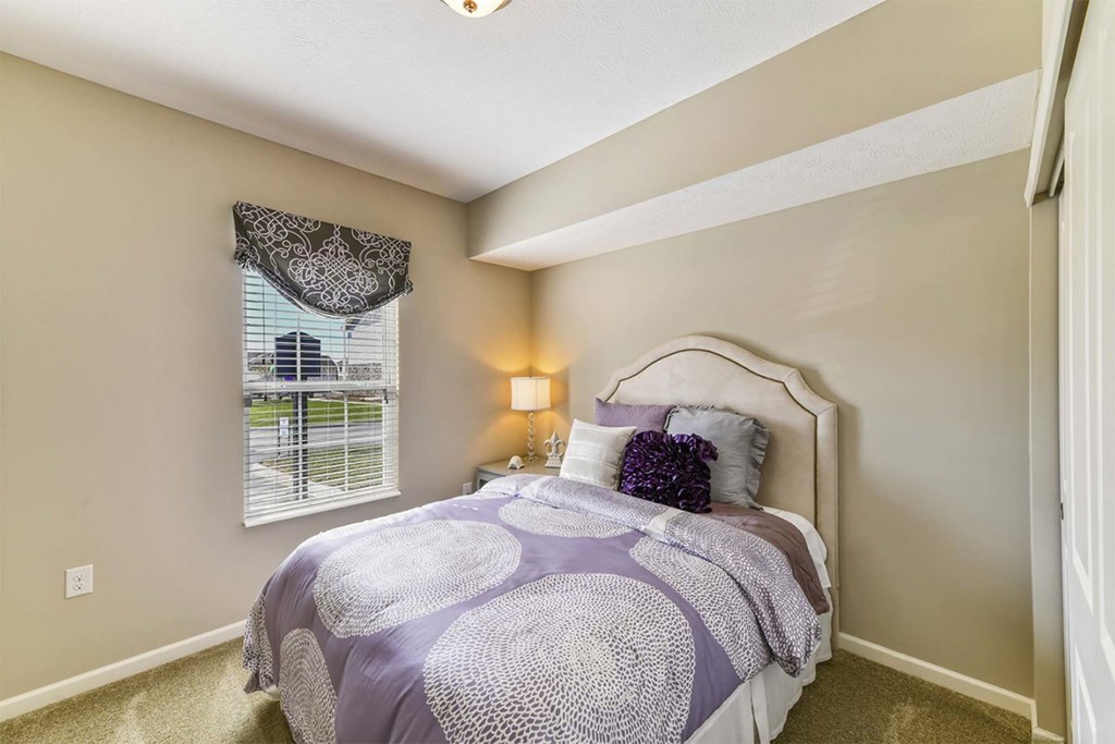 A bedroom with a bed covered in a purple and white comforter.