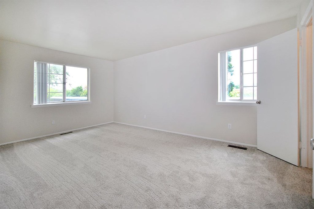 an empty bedroom with two windows and a carpeted floor