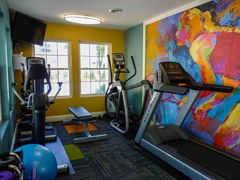 a gym with cardio equipment and a large painting on the wall