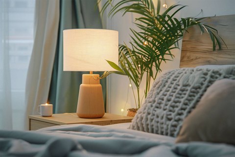 A bedroom scene with a bed, a lamp, a plant, and a lit candle.