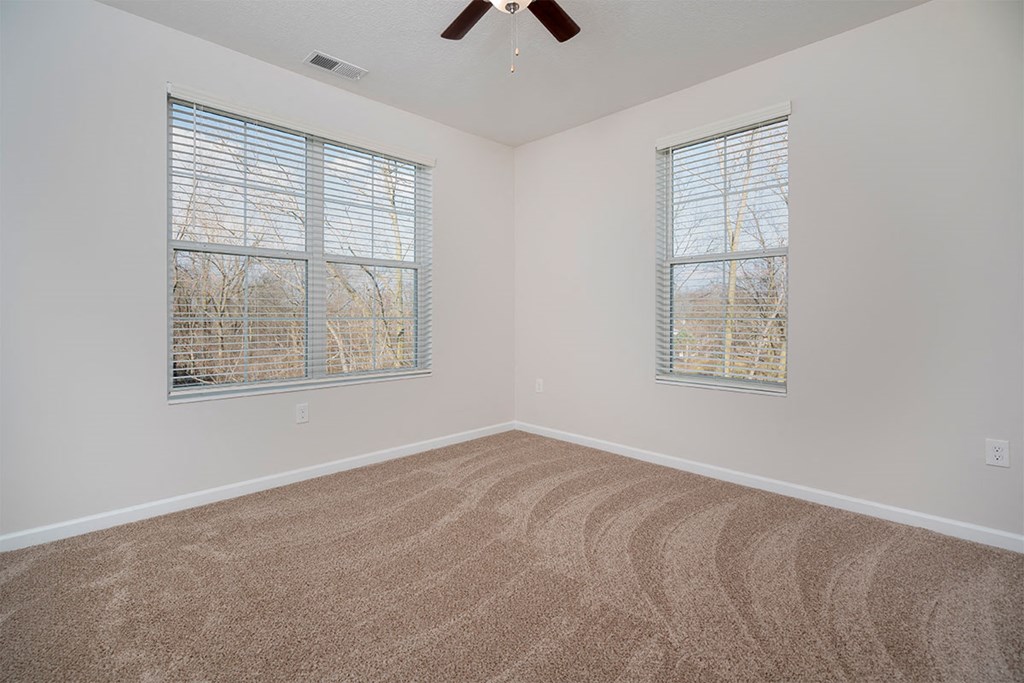 an empty room with two windows and a ceiling fan