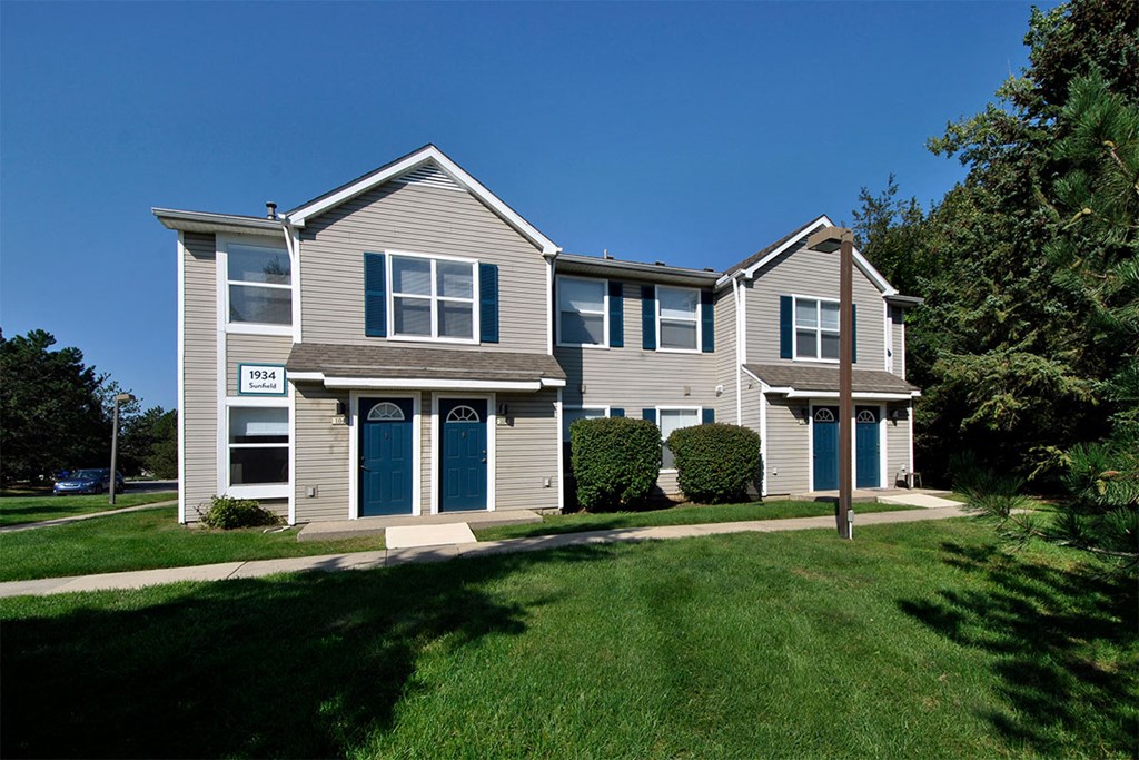 a tan house with blue doors on a lawn