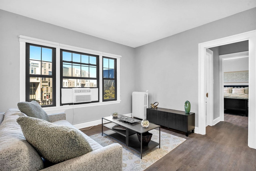 A living room with a grey couch, a coffee table, and a large window with a view of a building.