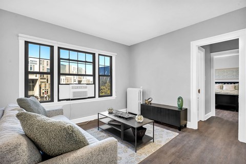A living room with a grey couch, a coffee table, and a large window with a view of a building.