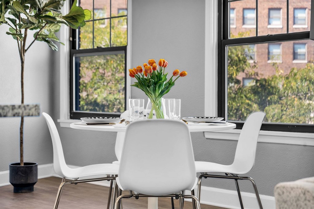 A dining table with chairs and a vase of flowers in front of a window.