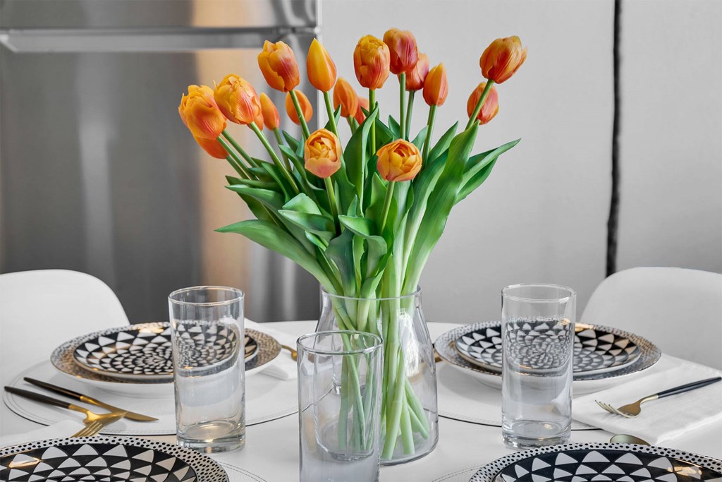 A table set with plates and glasses with a vase of orange tulips in the center.