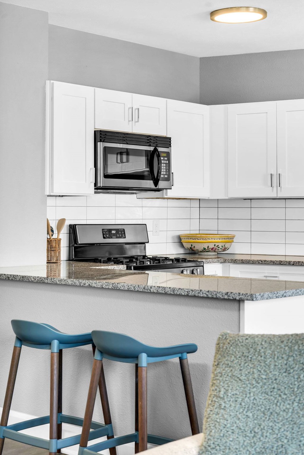 A kitchen with a microwave, stove, and blue barstools.