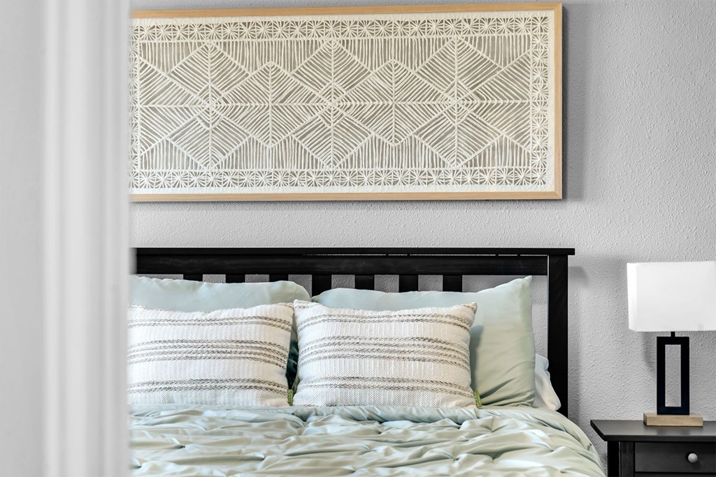 A bed with a black headboard and a white pillow with a geometric patterned artwork above it.