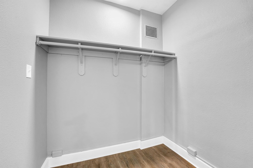 A white wall with a grey shelf and a wooden floor.