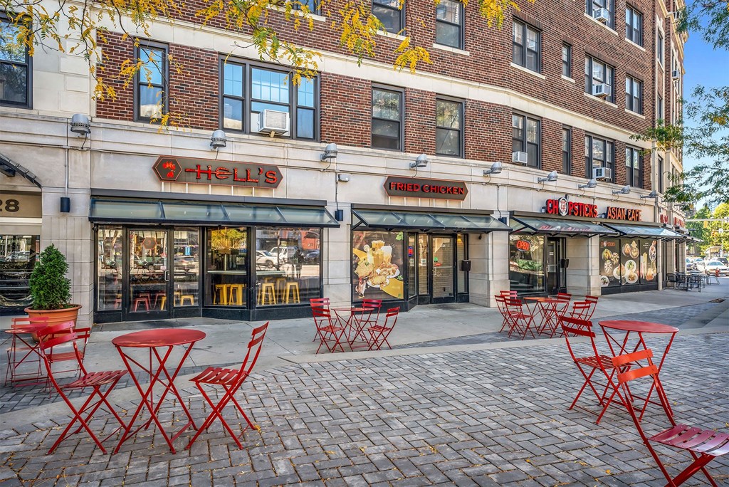A restaurant with red chairs and tables outside.