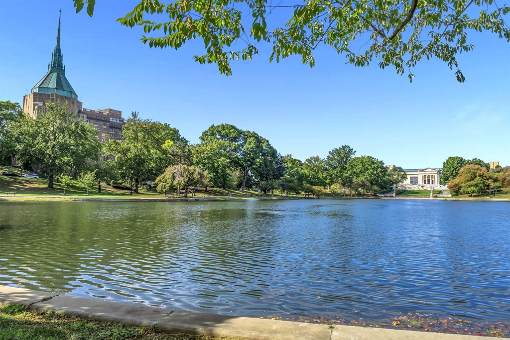A serene lake surrounded by lush greenery and a building with a green spire in the background.
