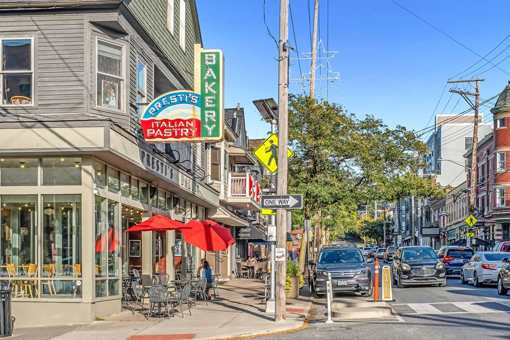 A street view of a city with cars parked on the side of the road and a bakery in the background.