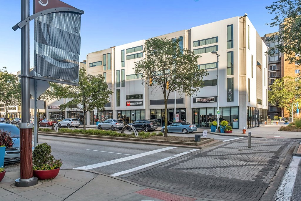 A street view of a city with a building in the background and a car parked on the side of the road.