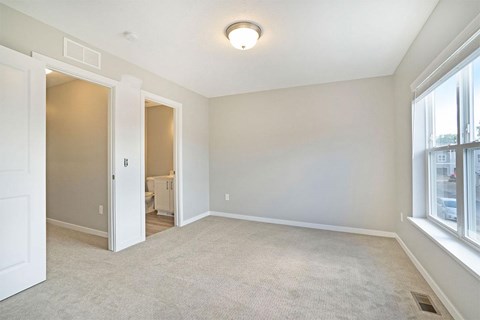A spacious room with a carpeted floor and a window on the right side.