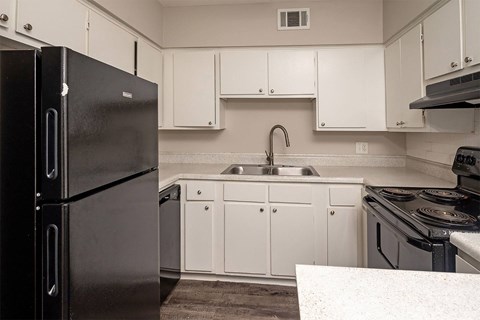 A black refrigerator stands in a kitchen with white cabinets and a sink.
