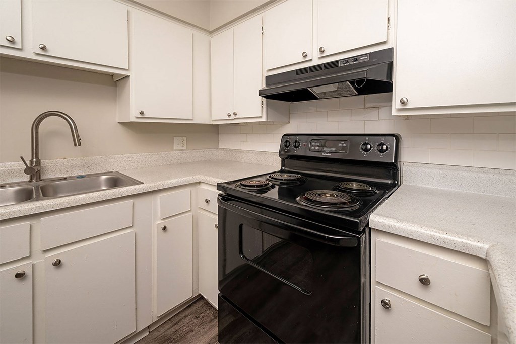 A black stove in a kitchen with white cabinets.
