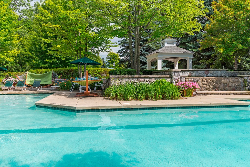 a swimming pool with a fountain and a poolside gazebo and trees