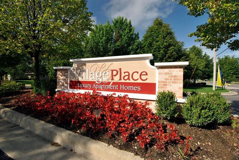 A sign for Village Place Luxury Apartment Homes is surrounded by red flowers.