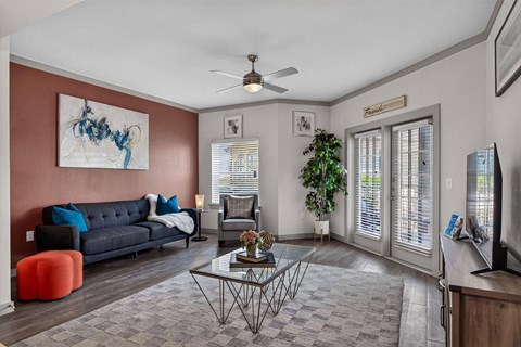 A living room with a grey sofa, a glass coffee table, a TV, and a painting on the wall.