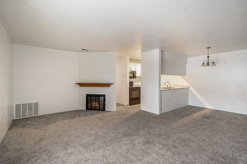 an empty living room with a fireplace and a kitchen