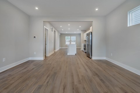 A spacious room with wooden flooring and a refrigerator on the right side.