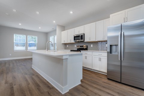 A modern kitchen with a stainless steel refrigerator and wooden flooring.