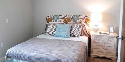 A bed with a white comforter and a pillow with a leaf pattern on it.
