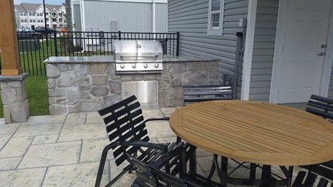 A patio with a table, chairs, and a grill.