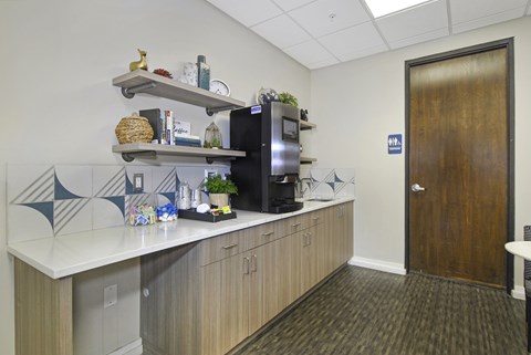 A kitchenette with a refrigerator, microwave, and a counter with a pineapple on it.