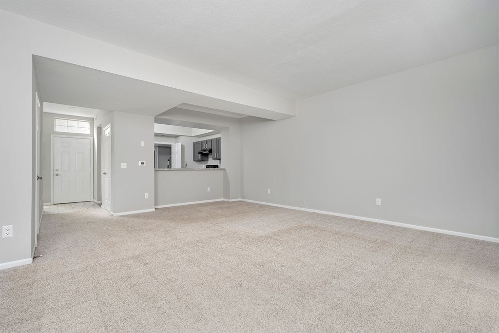 an empty living room with a kitchen in the background
