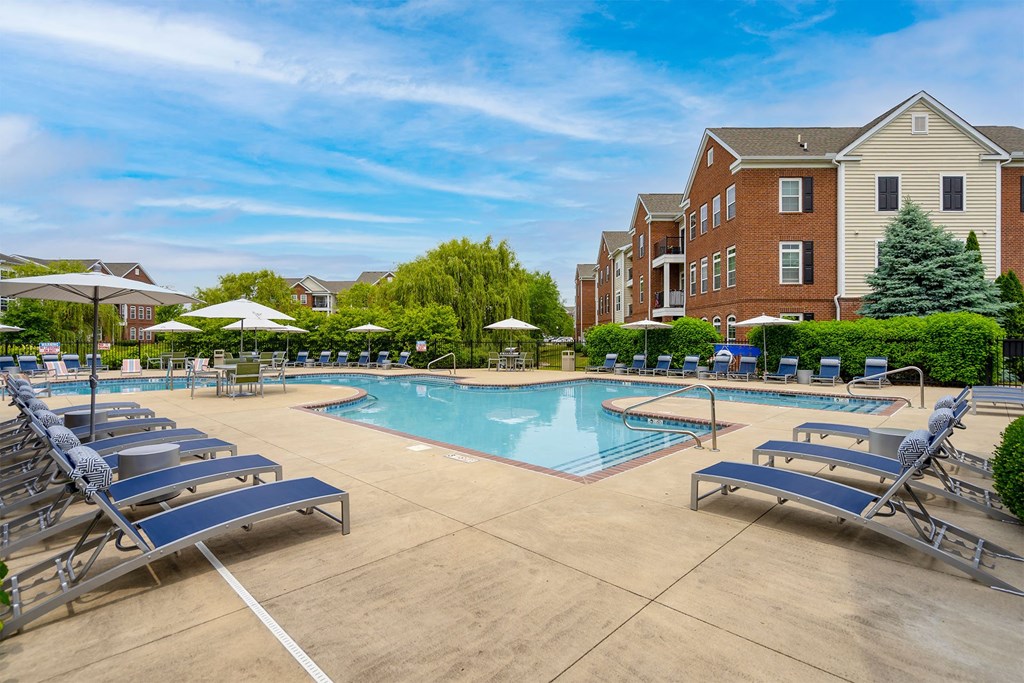 a swimming pool with chaise lounge chairs and umbrellas in front of a brick building