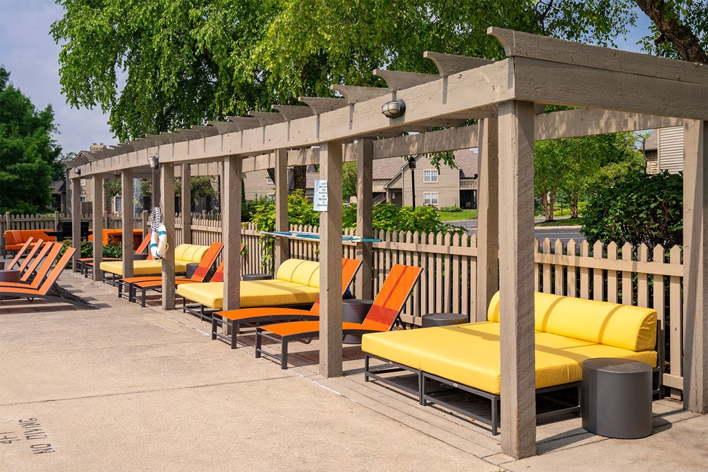 a row of orange and yellow lounge chairs under a wooden pergola