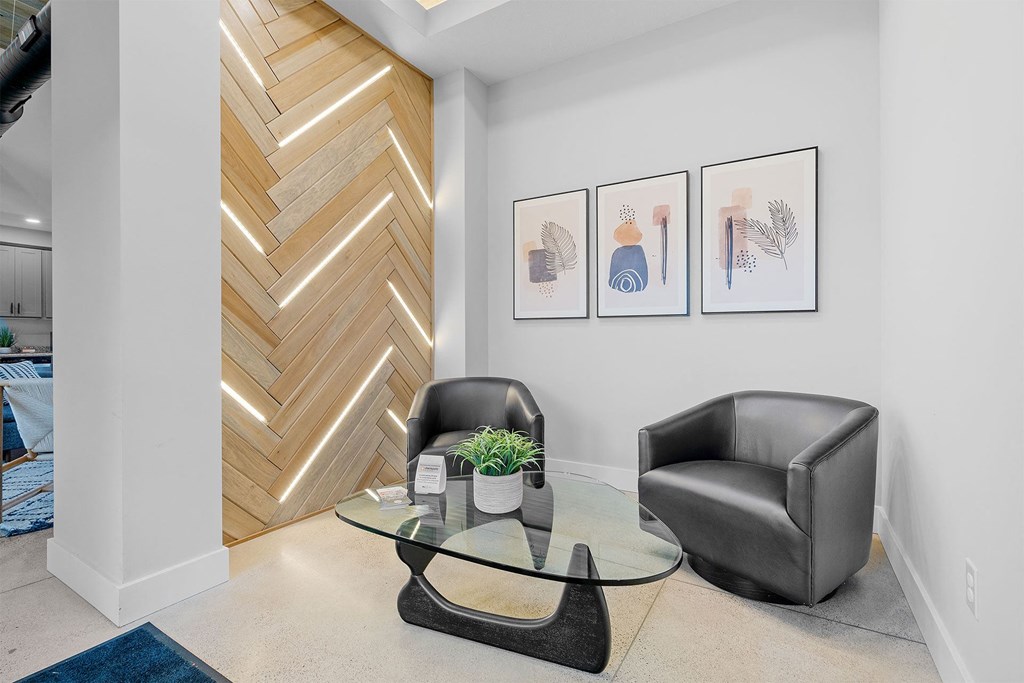 a living area with a glass coffee table, two black chairs, a chevron wood