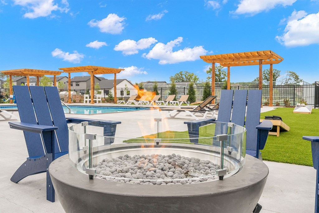 a fire pit with blue chairs around it near a pool