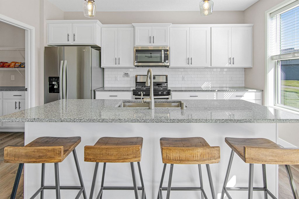 a kitchen with white cabinets and a white island with three wooden stools