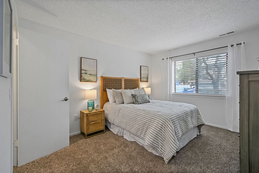 A bedroom with a bed, nightstand, and two pictures on the wall.