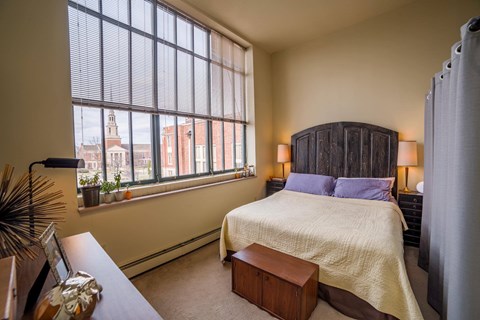 A bedroom with a large bed and a window overlooking a cityscape.